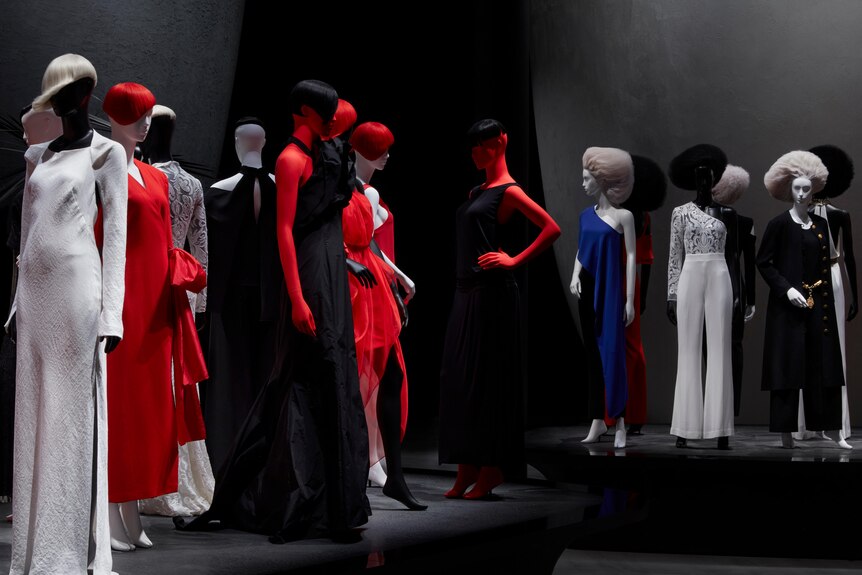 Two podiums in a gallery space that feature multiple mannequins dressed in red, white and black garments.