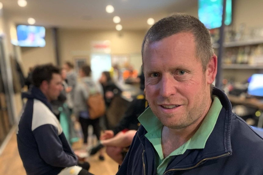 A man in a blue jacket in a bar with a beer in hand.