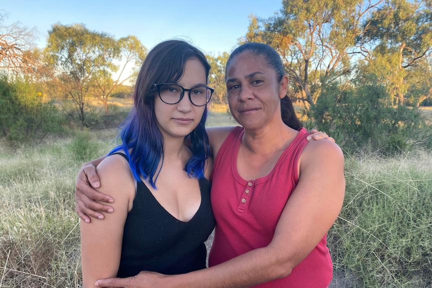 An Indigenous mother stands with her arms around her teenage daughter
