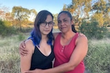 An Indigenous mother stands with her arms around her teenage daughter.