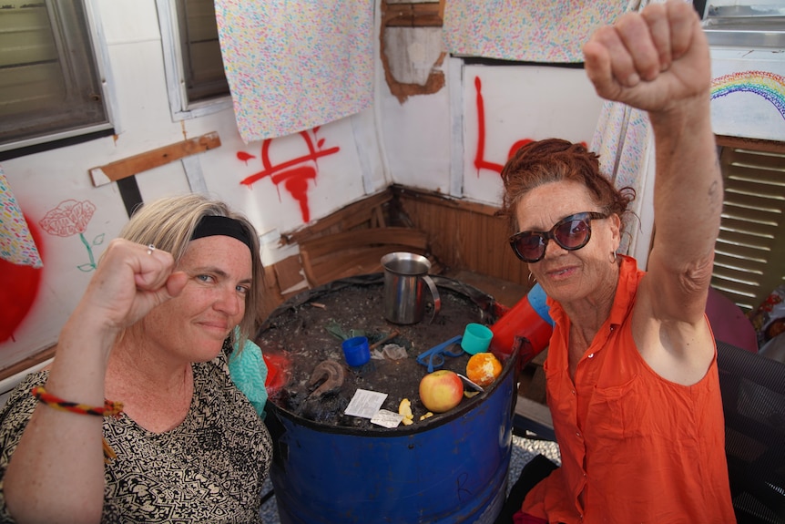 Two women holding one fist in the air while the other arm is locked in a concrete barrel. 