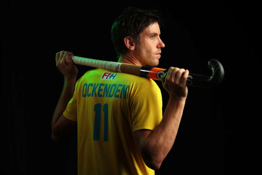 Eddie Ockenden holds a hockey stick over his shoulder and looks aside in a posed portrait photo.