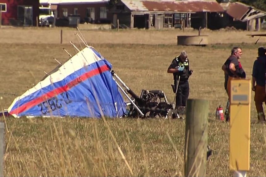 Crumpled paraglider in a paddock with emergency service workers staring near the wreckage.