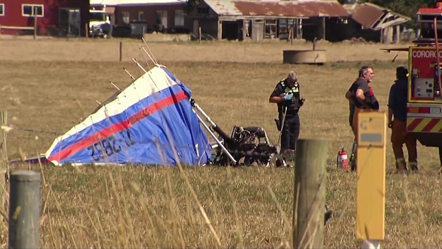 Crumpled paraglider in a paddock with emergency service workers staring near the wreckage.