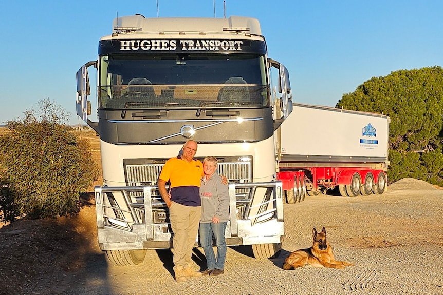 A couple and their dog in front of a truck.