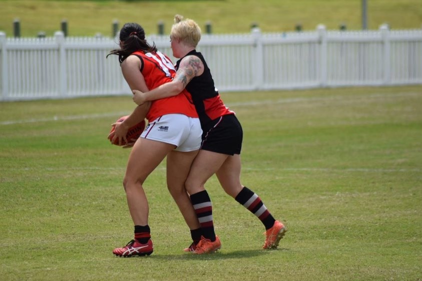 A girl being tackled while holding a football. 