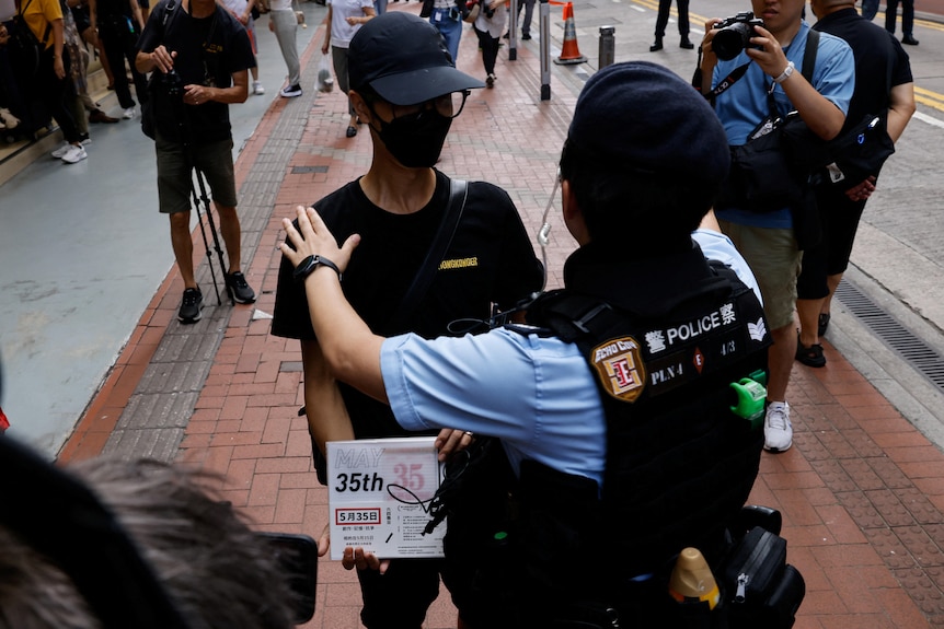 A police officer stands in front of a man who is dressed in black and holds a sign that says 'May 35'. 