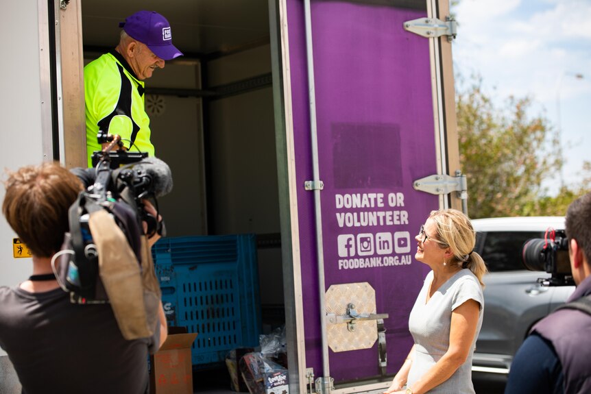 A woman in a grey shirt stands in front of a purple truck