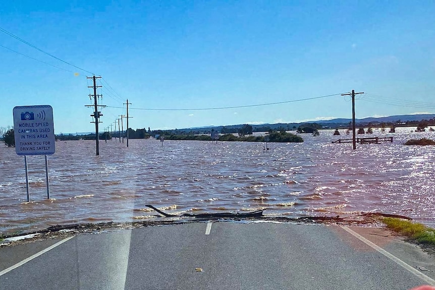 A road covered in floodwater with submerged power poles