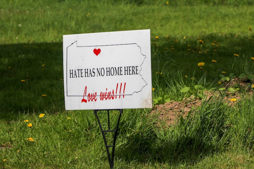 A sign stuck in grass reading "hate has no home here. Love wins"