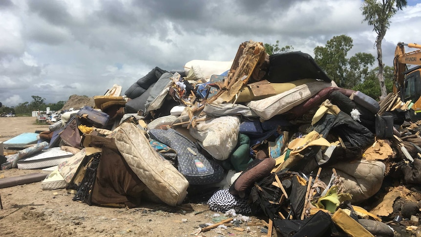 Piles of dirty mattresses among debris at a tip.