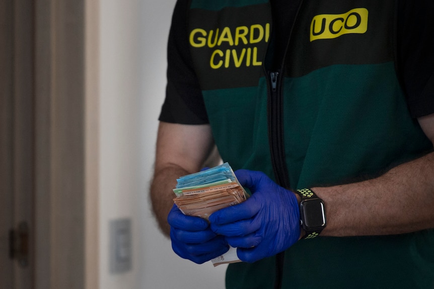 Close up of a police officers hands in blue gloves holding a wad of cash. 