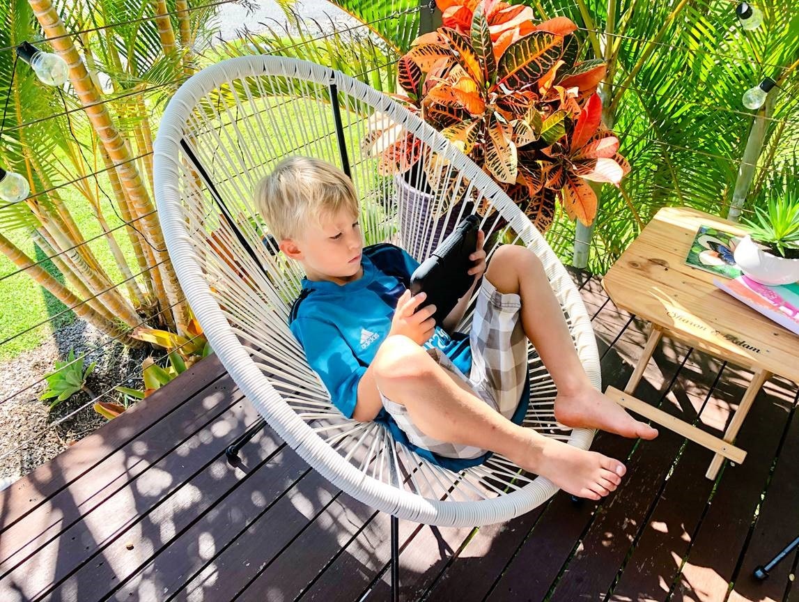 Boy sits on outdoor chair looking at ipad