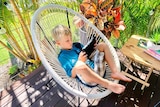 Boy sits on outdoor chair looking at ipad.