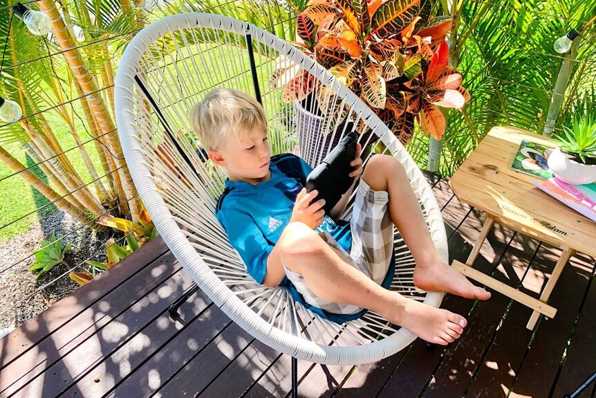 Boy sits on outdoor chair looking at ipad