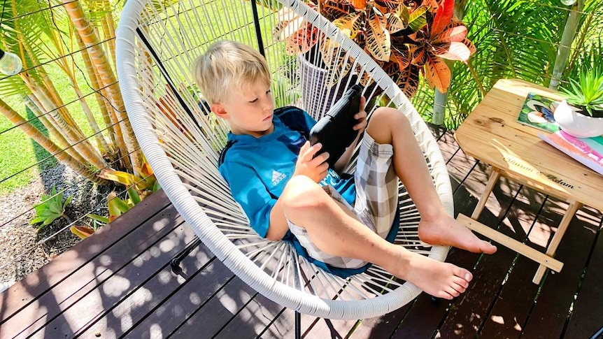 Boy sits on outdoor chair looking at ipad.