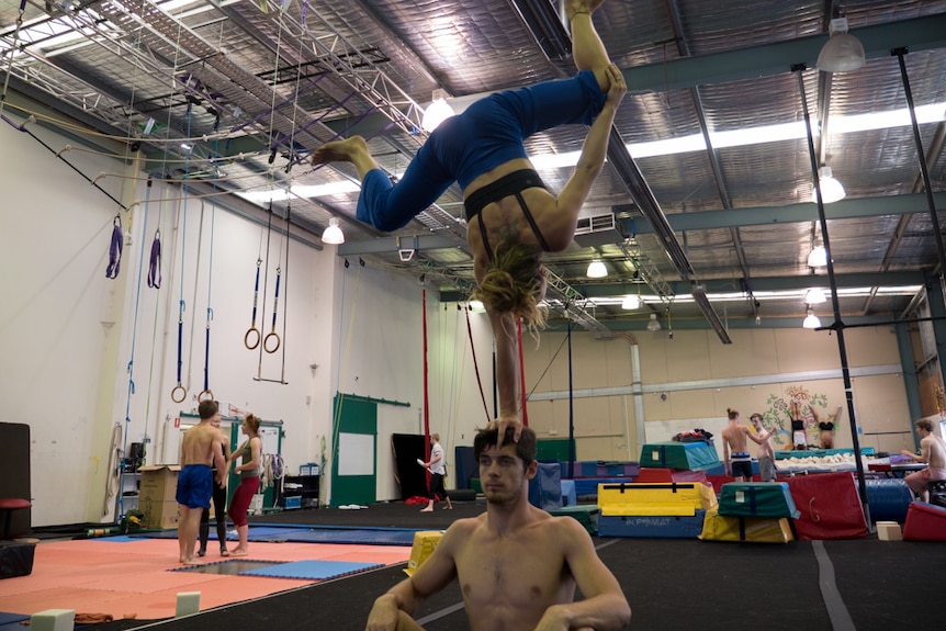 Rhiannon Cave-Walker and Dan Cave-Walker in seated single handstand.
