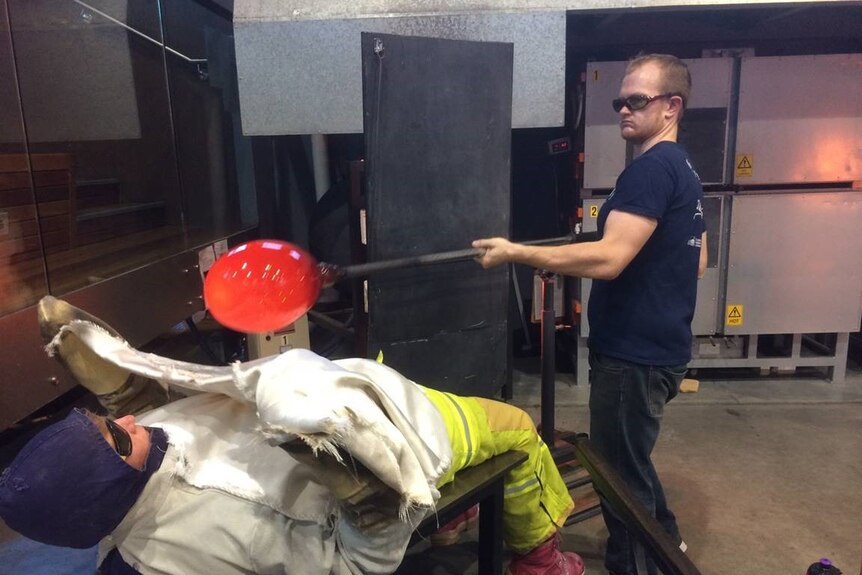 Catherine lies down wearing protective gear as a glass-blown balloon-like object is passed to her to hug into shape.