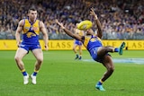 An AFL player leaning backwards has his eyes locked on the ball as he gets ready to take a mark.