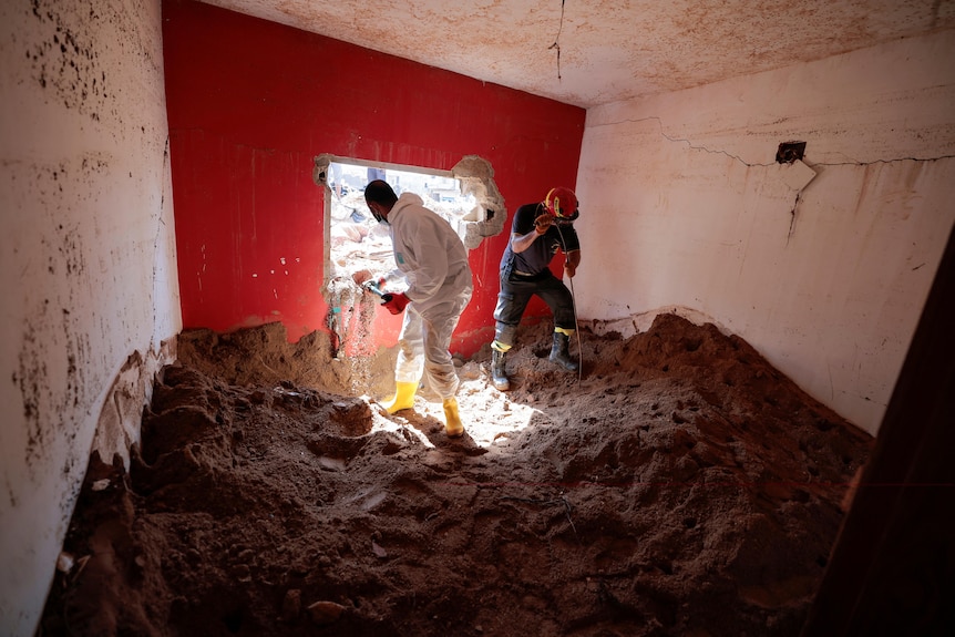 Rescuers dig in high mud that innundates a room  