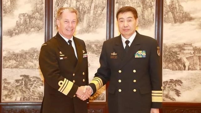 Vice Admiral Tim Barrett and Shen Jinlong, both wearing navy garb, shake hands and look at the camera.