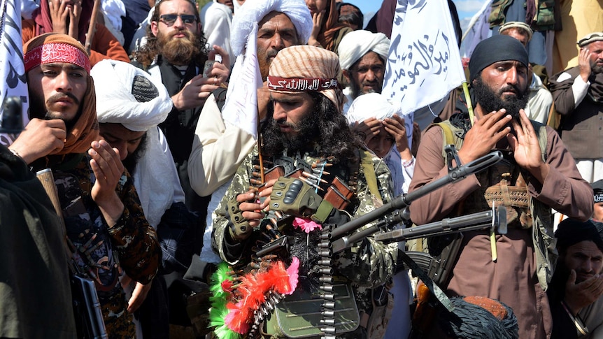 Men in Afghan cloths carrying rifles, belt of bullets and flags with Afghan writting.