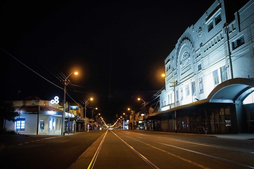 A long stretch of empty tram tracks in Melbourne at night with streetlights.