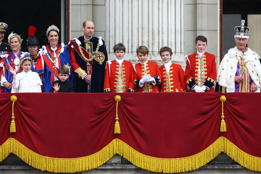 The royal family, dressed in formal regalia, stand on the balcony of Buckingham Palace.