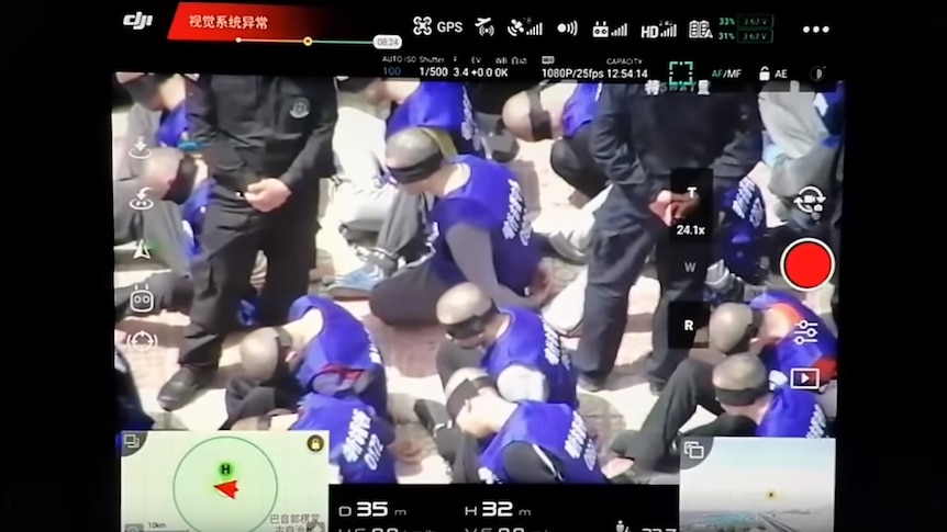 A screenshot from the YouTube video shows police in black standing over purportedly Uyghur Muslim men.