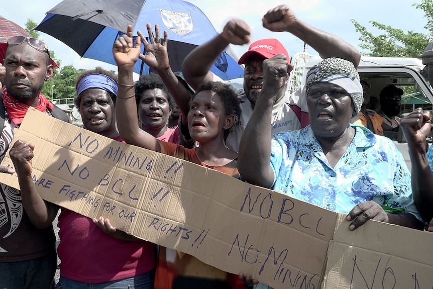 Panguna mine protesters wave their hands and fists in the air and hold a sign that says "No Mining! No BCL!" at a roadblock.