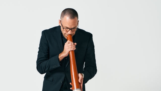 Chris Williams playing didgeridoo against a white background