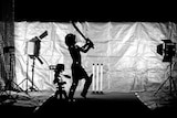 A child swings a cricket bat surrounded by camera gear and lights.