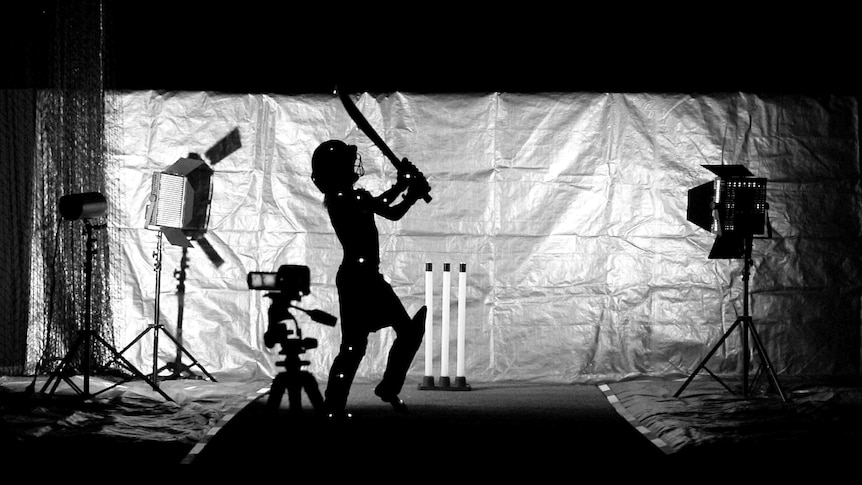 A child swings a cricket bat surrounded by camera gear and lights.