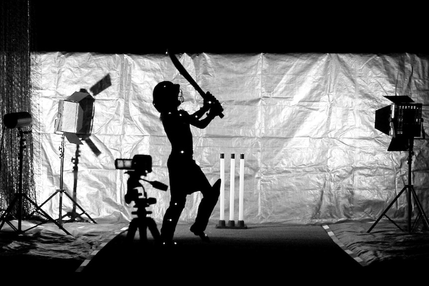 A child swings a cricket bat surrounded by camera gear and lights.