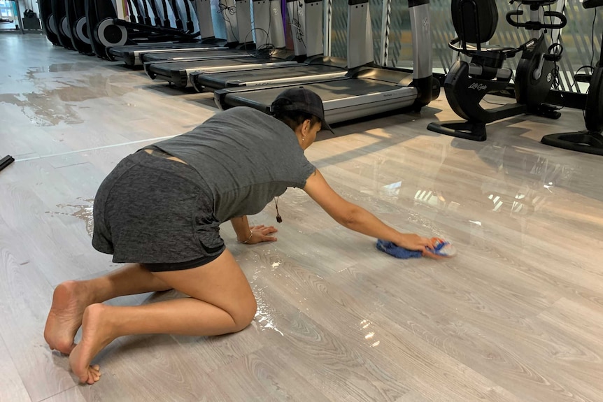 Delyse Edwards on her hands and knees mopping up water with a rag.