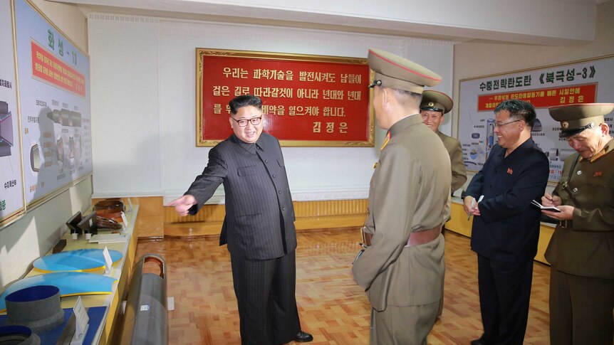 Kim gestures towards a table at a defence academy. Experts say the diagram to his left shows a powerful new missile design.