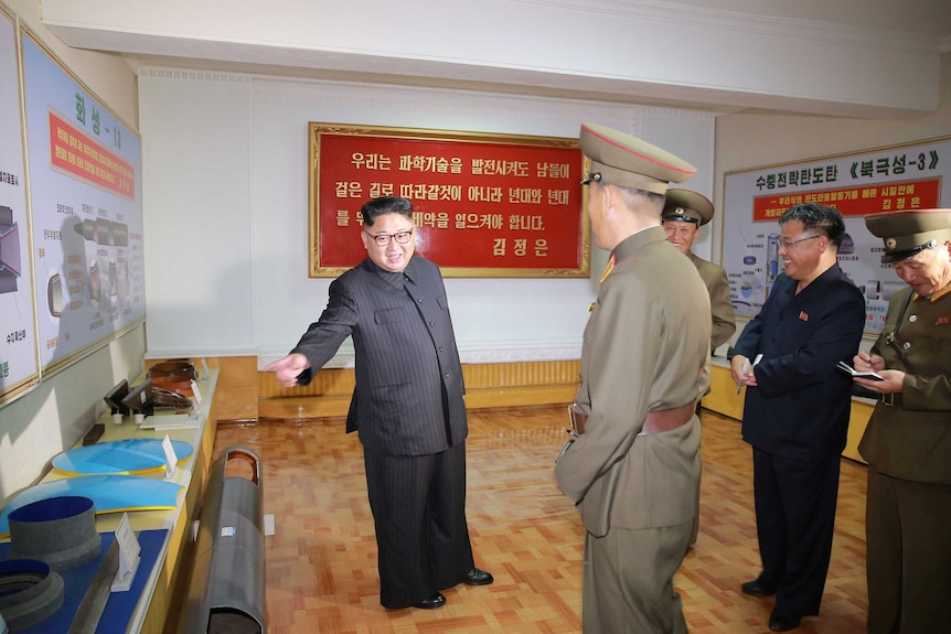 Kim gestures towards a table at a defence academy. Experts say the diagram to his left shows a powerful new missile design.