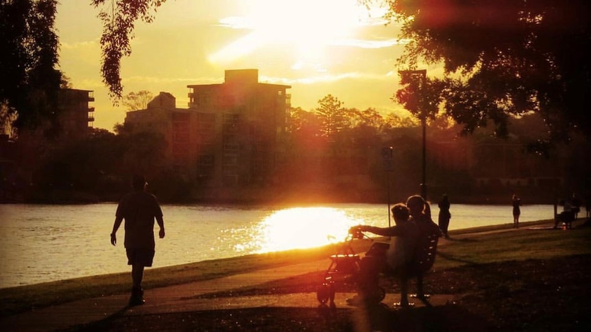 Sun shimmers across Brisbane River as people walk along pathway at West End in March 2019.