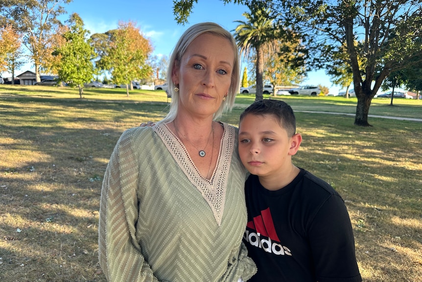 Liana standing in a park with her arm wrapped around her son who is leaning into her.