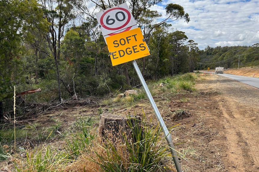 Tire marks in the dirt on the side of a road near a stump and bent speed sign.