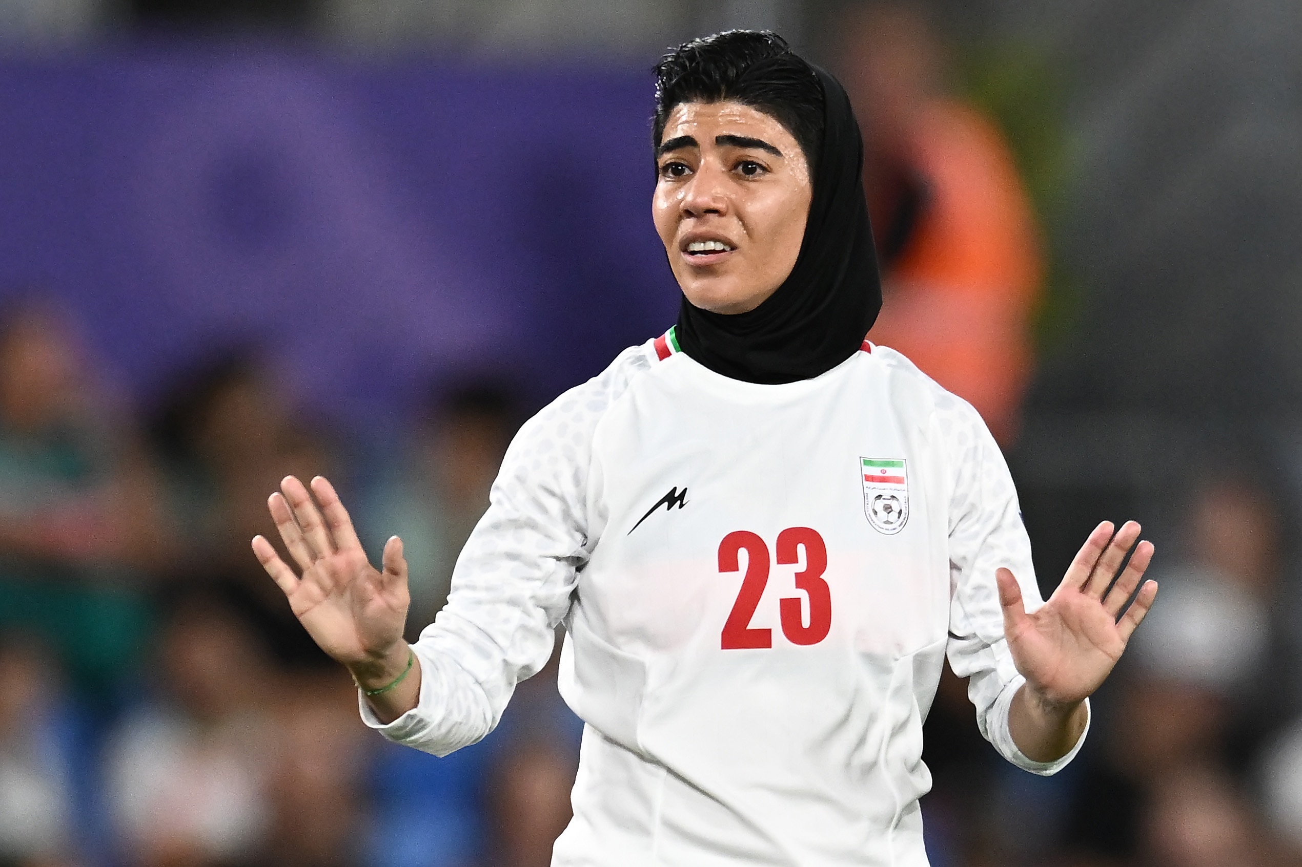 Um membro da seleção iraniana de futebol feminino estende as duas mãos durante um jogo, tentando pedir calma 