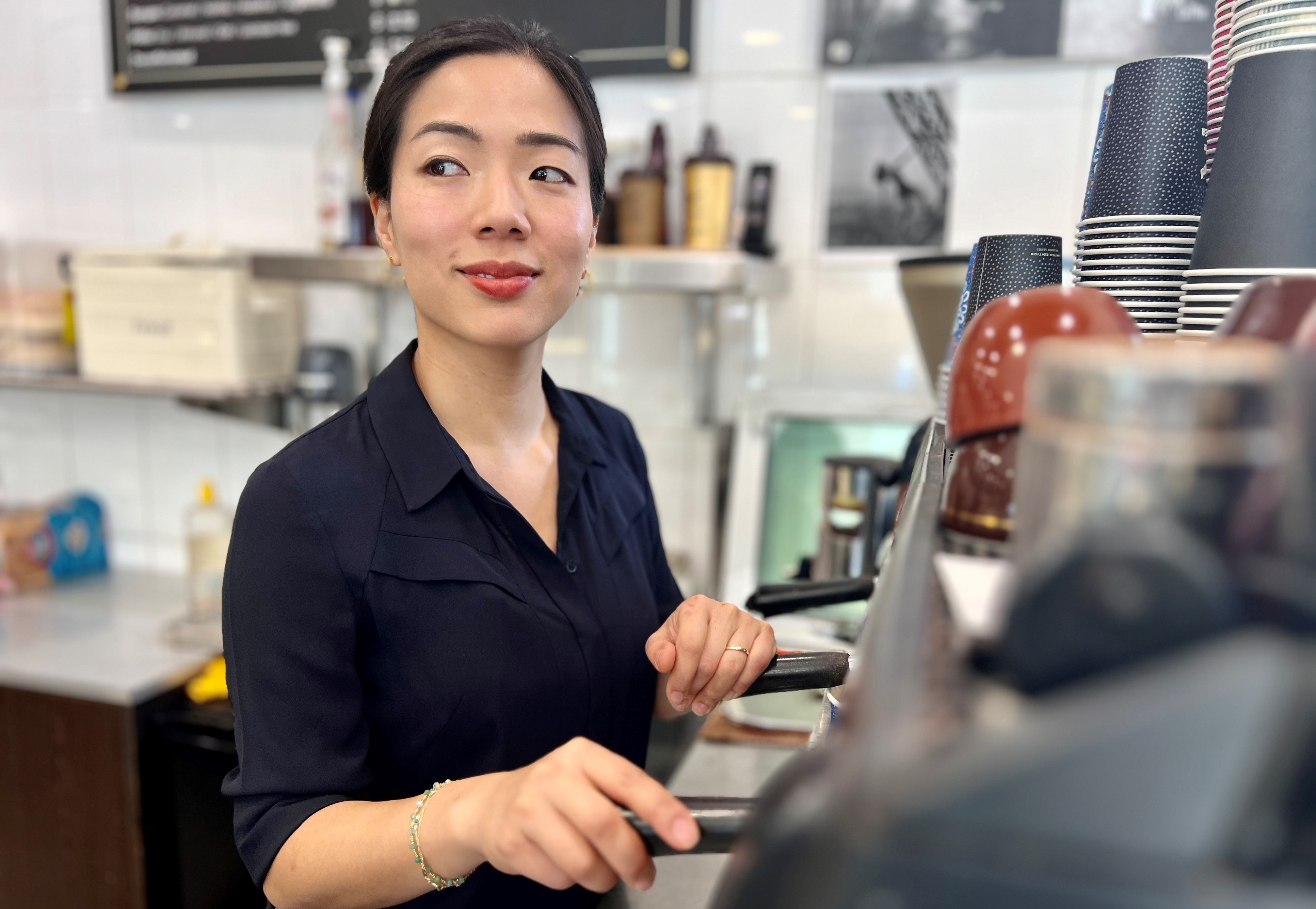 An Asian woman standing behind a coffee machine.