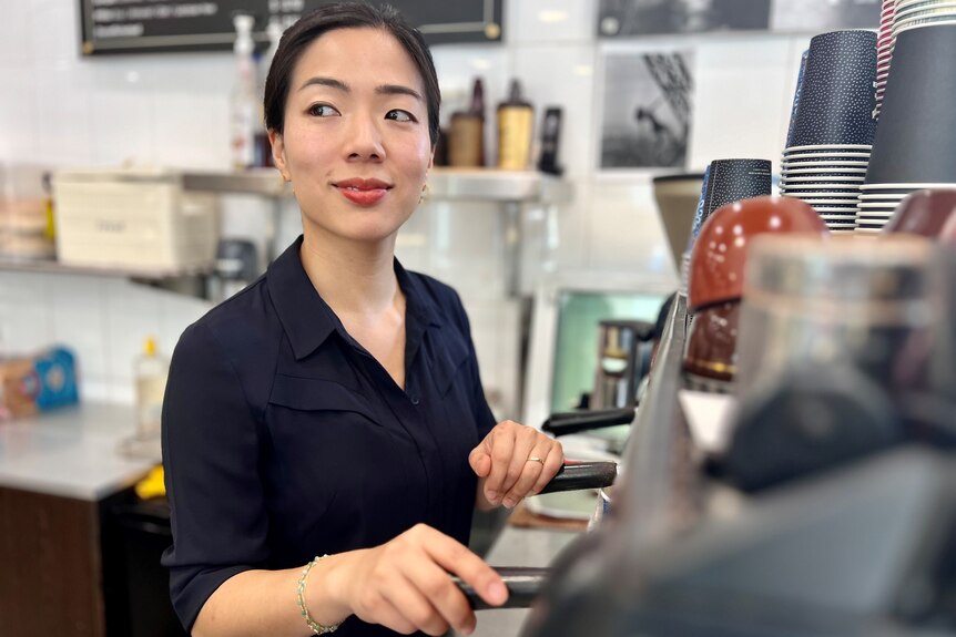 An Asian woman standing behind a coffee machine.