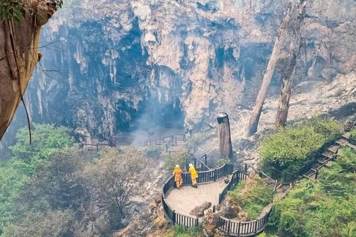 Firefighters stand on the ledge of a lookout overlooking the entrance to a cave