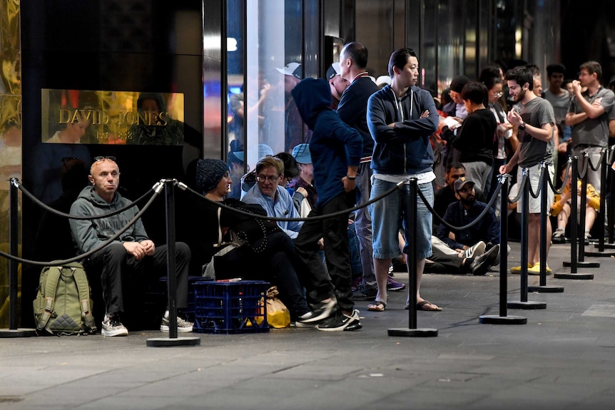 A line of people wait outside a David Jones store in the dark.