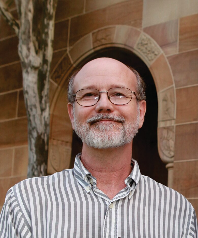 a man standing in front of a sandstone building smiles at the camera