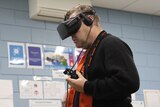 A man in a black jumper wearing virtual reality goggles holds a gaming controller.