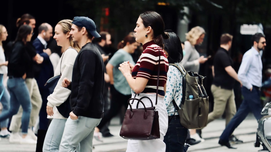 People cross the road at an intersection in a busy CBD.