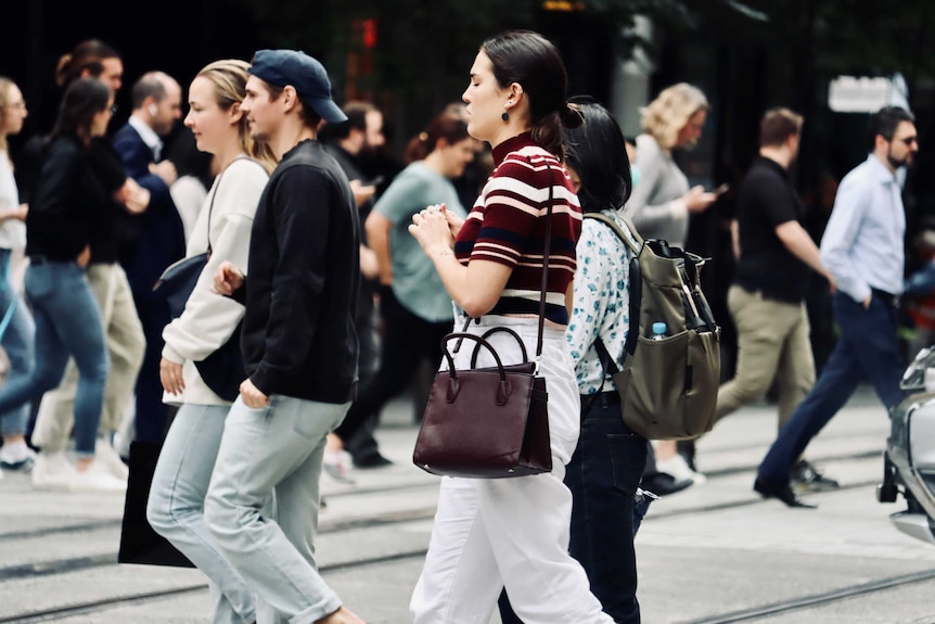 People cross the road at an intersection in a busy CBD.