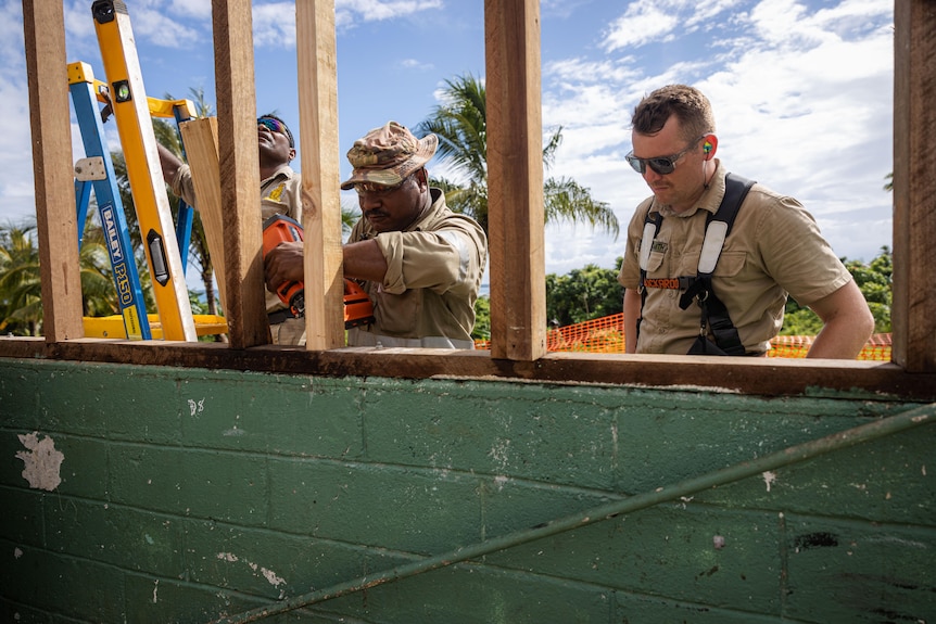 Two PNG soldiers work with an Australia soldier to build window frames in a green Besser block.